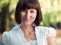 Woman with short hair and bangs, standing outside, smiling.