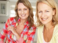 Two women sitting in a well lit room, smiling at the camera. 