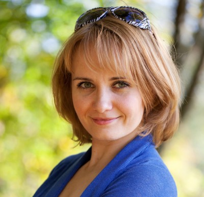 Woman with sunglasses on her head, standing outside smiling at the camera.