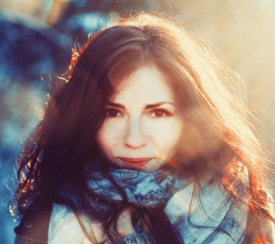 Woman softly smiling at the camera, wearing a plaid scarf. Image has a colourful, slightly blurry filter. 